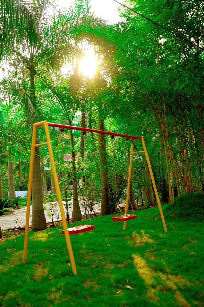 Rosewood Villas Pench garden swing under palm trees in a shaded seating spot.